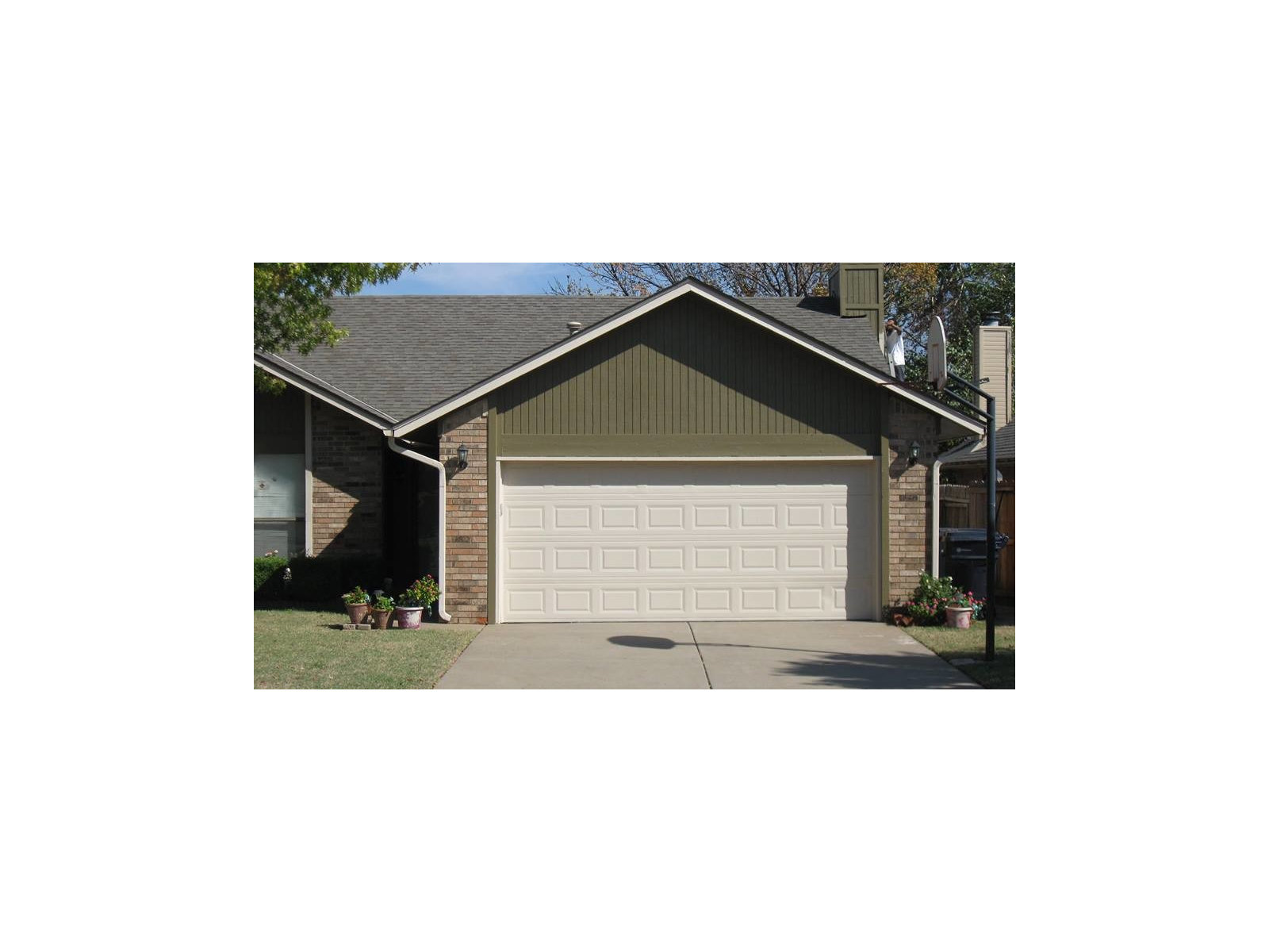 Low brick ranch home with a broad lawn, roofline and driveway in bright daylight.